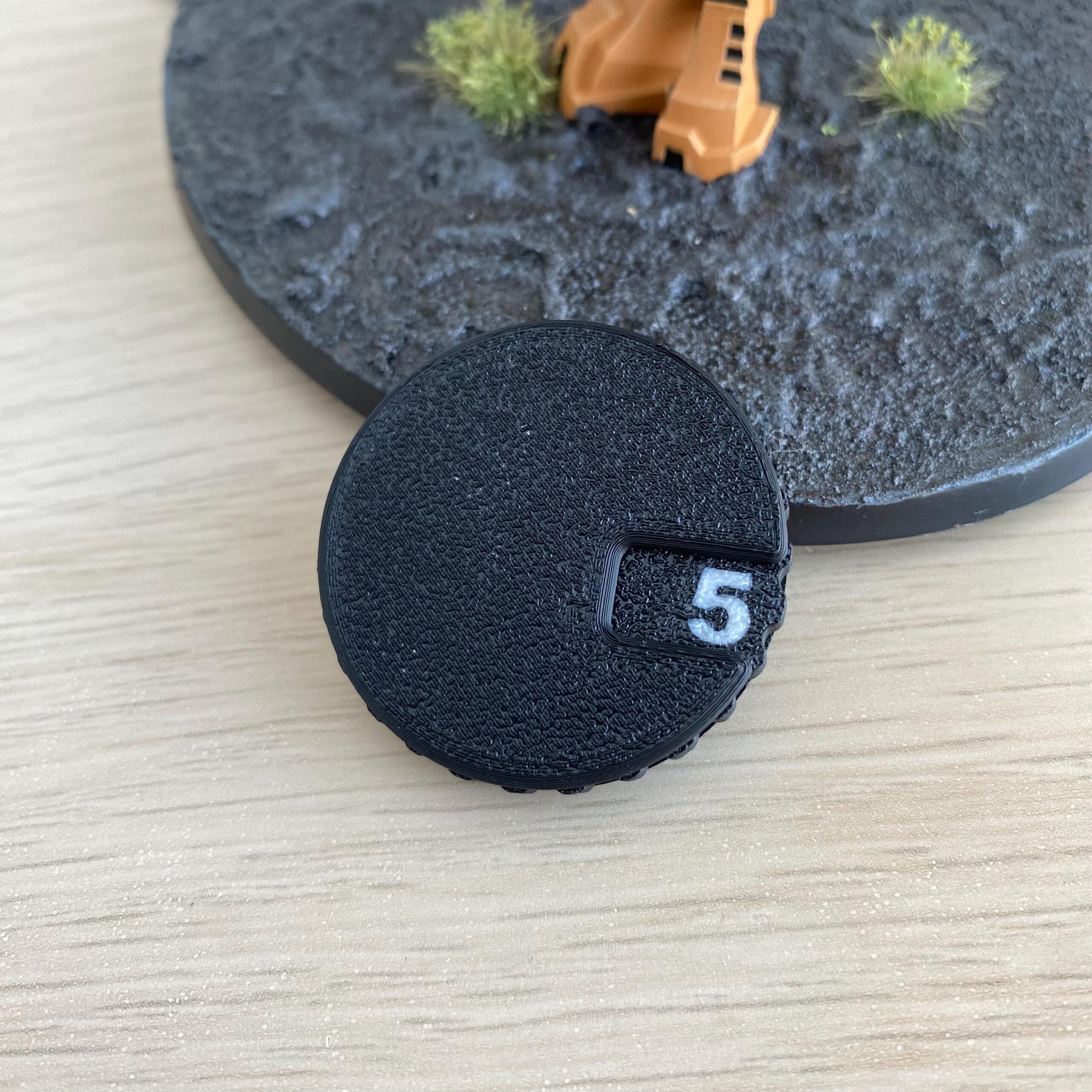 A circular black textured token featuring a white number 5 printed in a small rectangular inset.