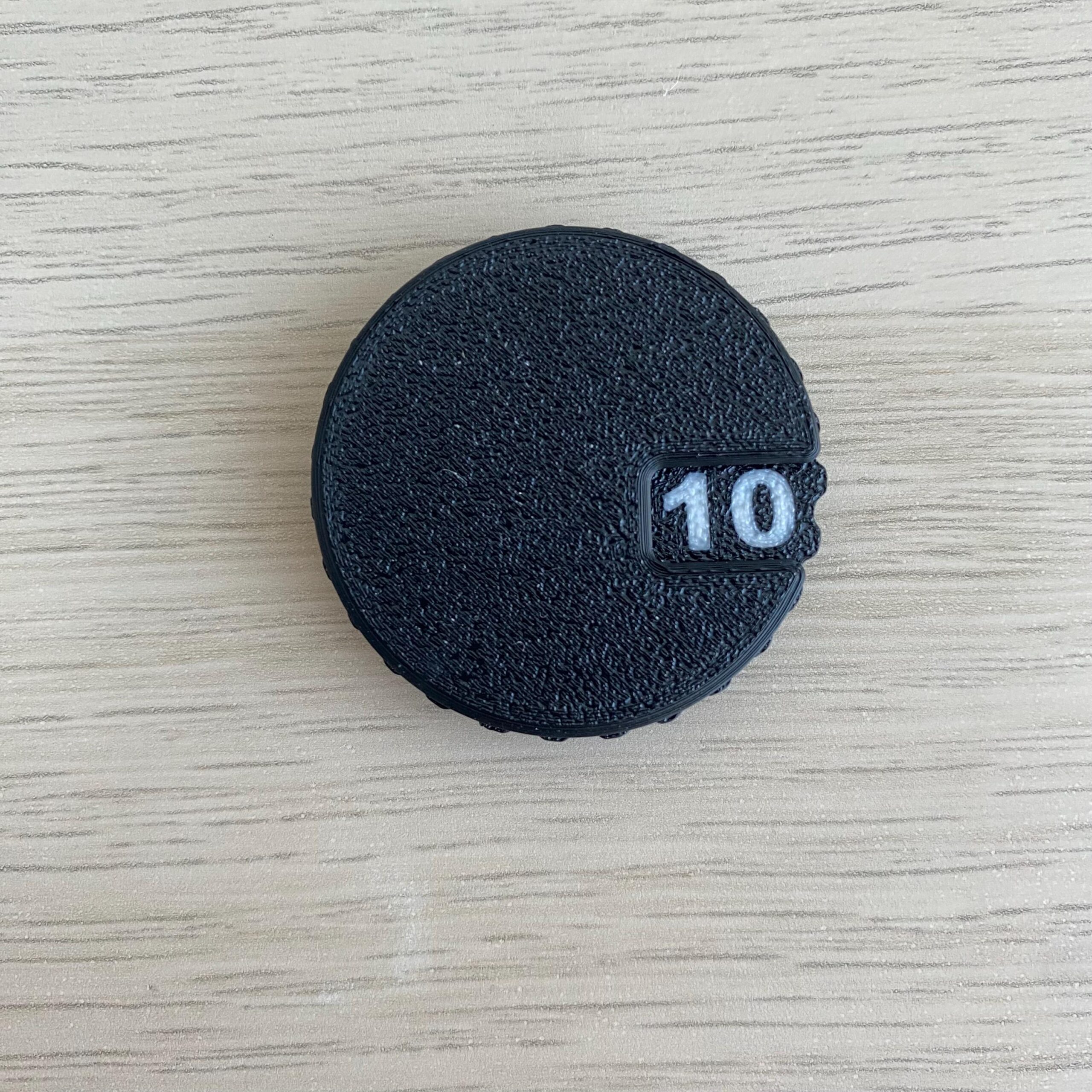 A circular black object with a textured surface and a small rectangular cutout on the right side.