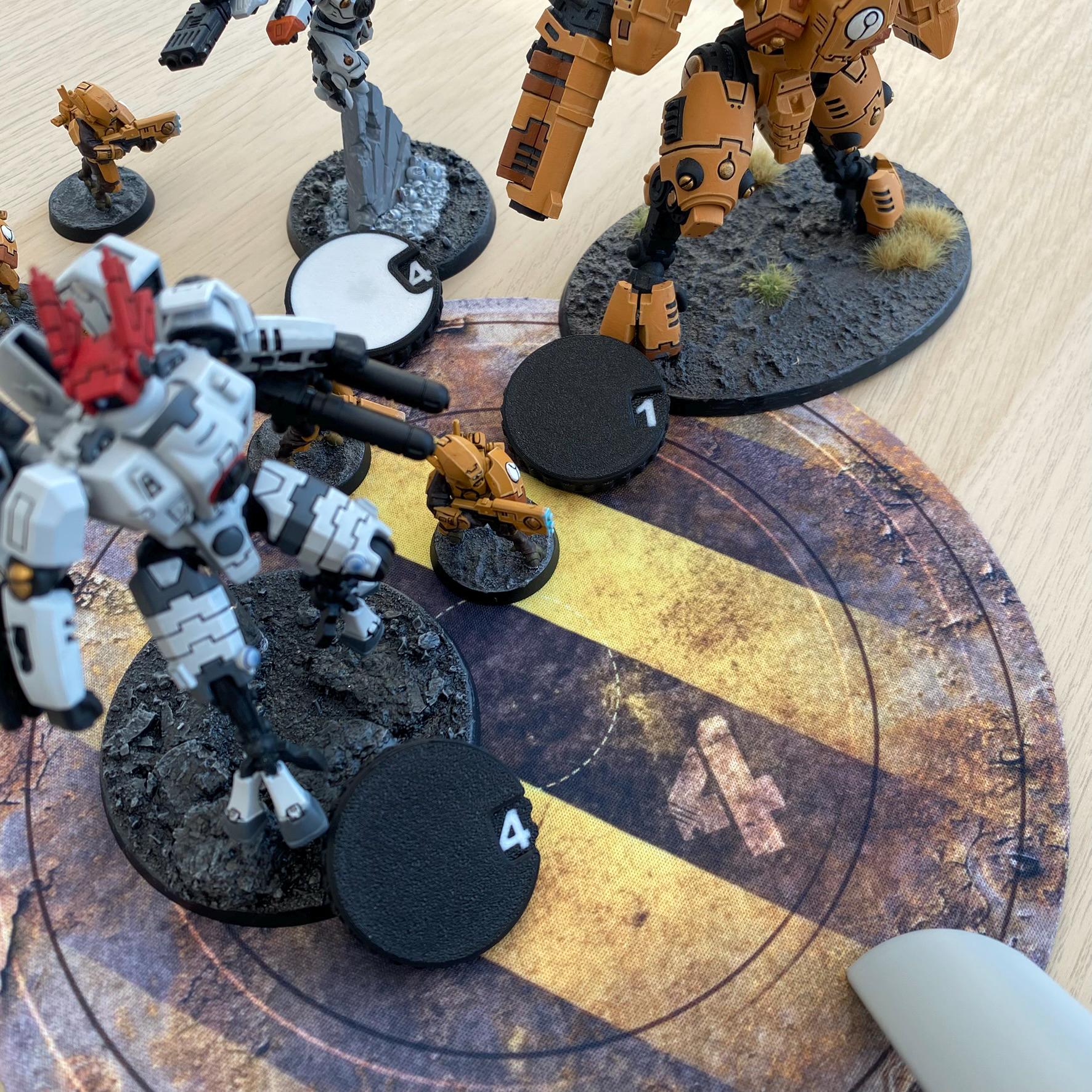 A collection of painted miniature robot figures in white, orange, and grey colour schemes, standing on textured circular bases.
