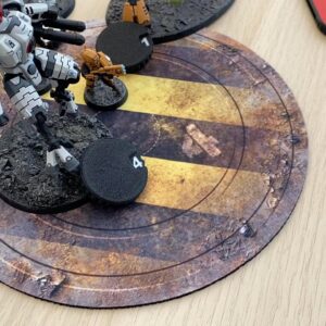 A white and grey mechanical robot miniature stands on a textured base next to a black circular token marked with the number 4.