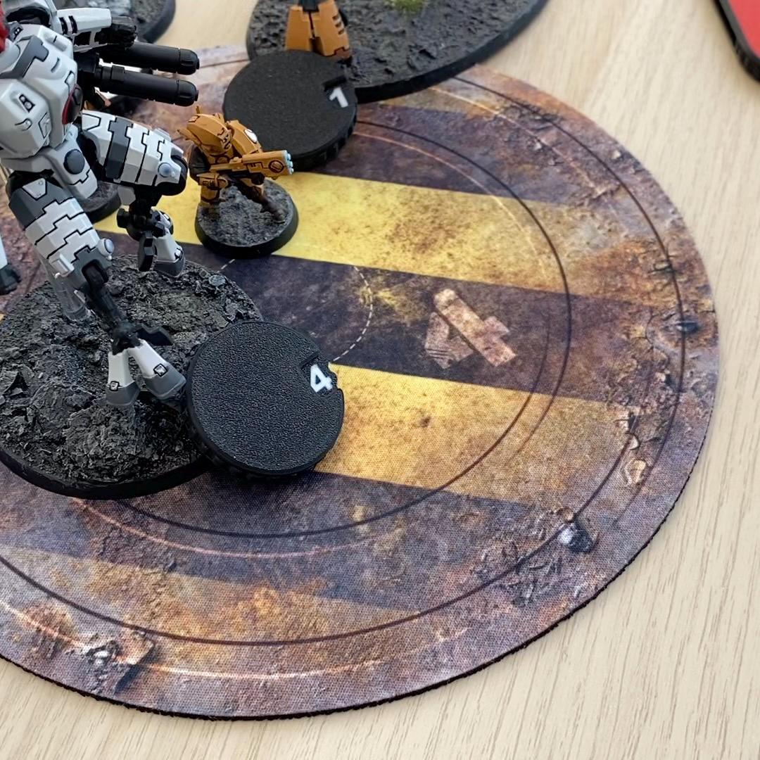 A white and grey mechanical robot miniature stands on a textured base next to a black circular token marked with the number 4.