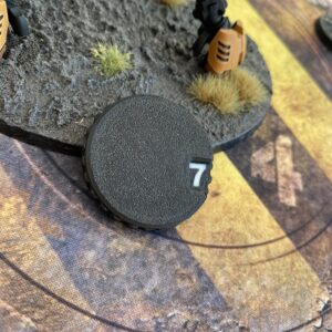 A circular black plastic gaming token featuring a textured surface and a white number seven printed in a small rectangular window on the right side.