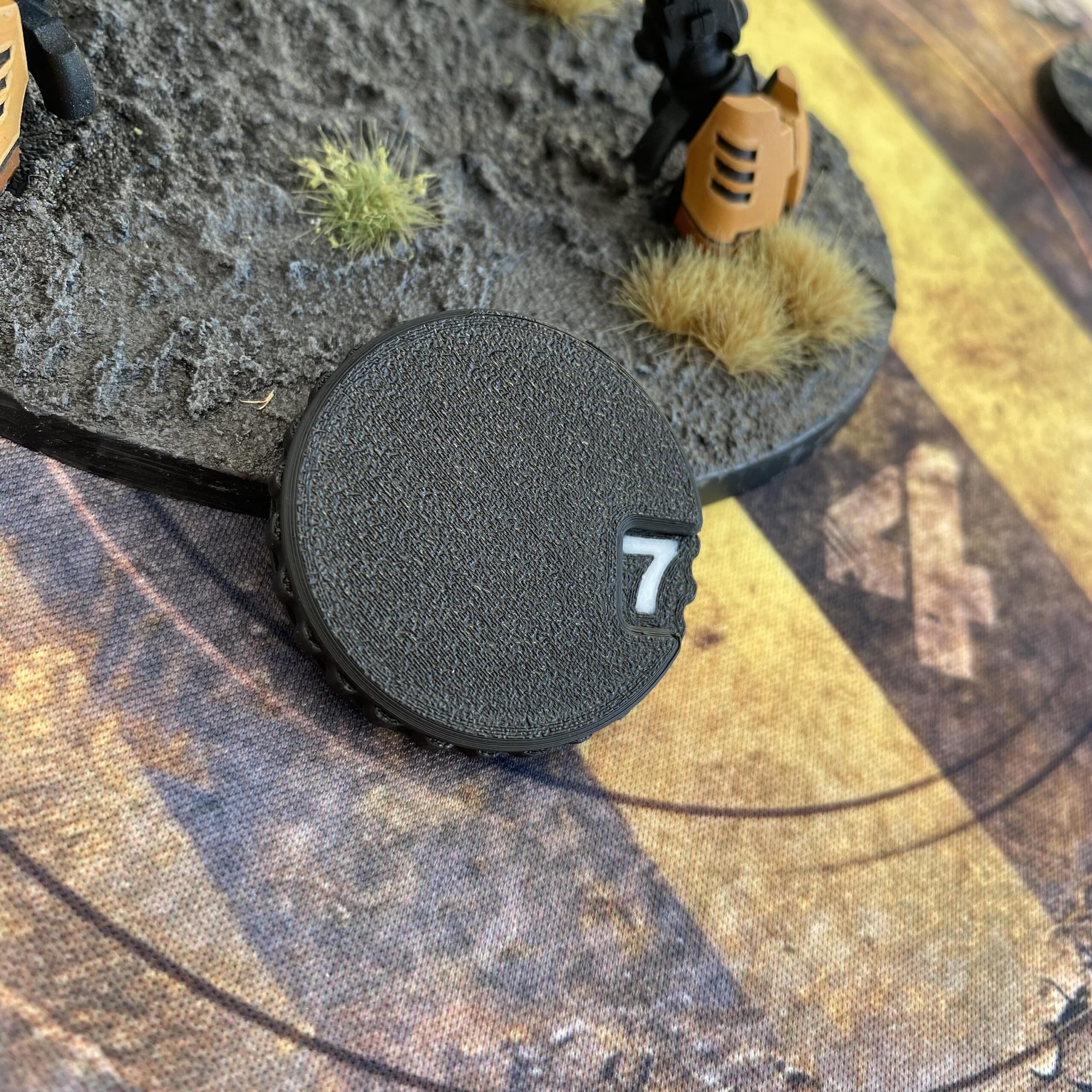 A circular black plastic gaming token featuring a textured surface and a white number seven printed in a small rectangular window on the right side.
