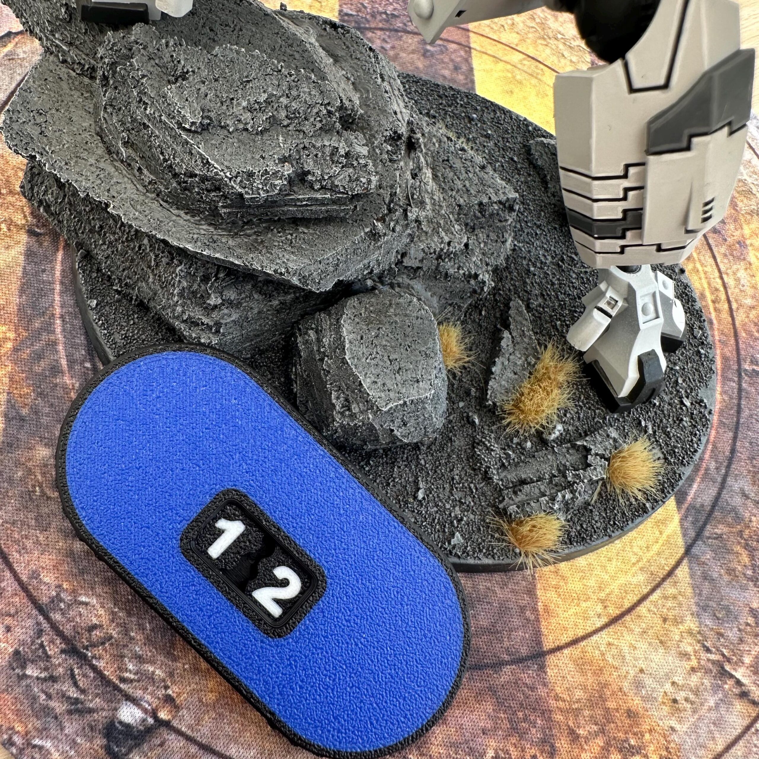 A white and grey robotic leg stands on a textured grey rocky base with small patches of brown grass.