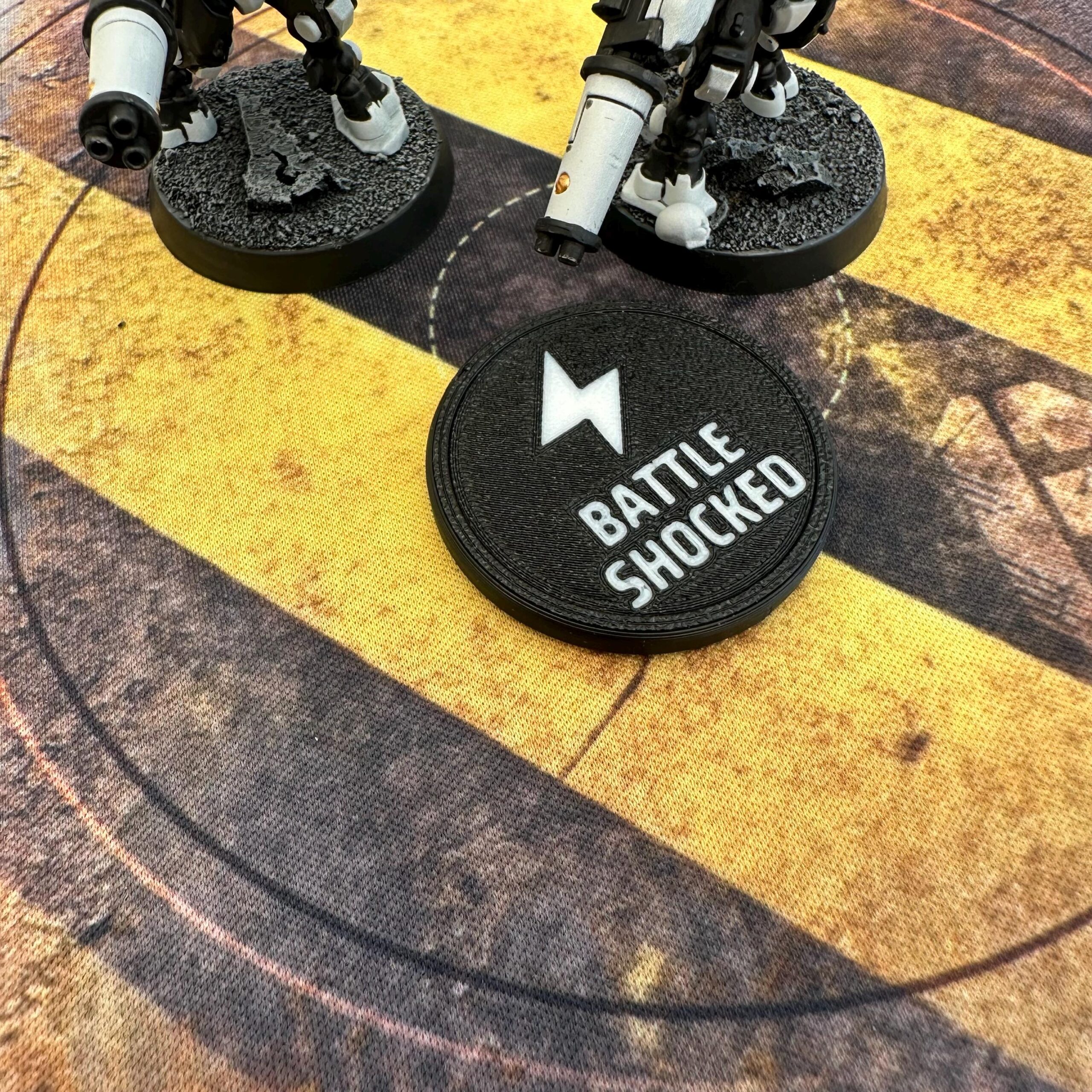 A circular black token featuring a white lightning bolt icon and the text BATTLE SHOCKED printed in white.
