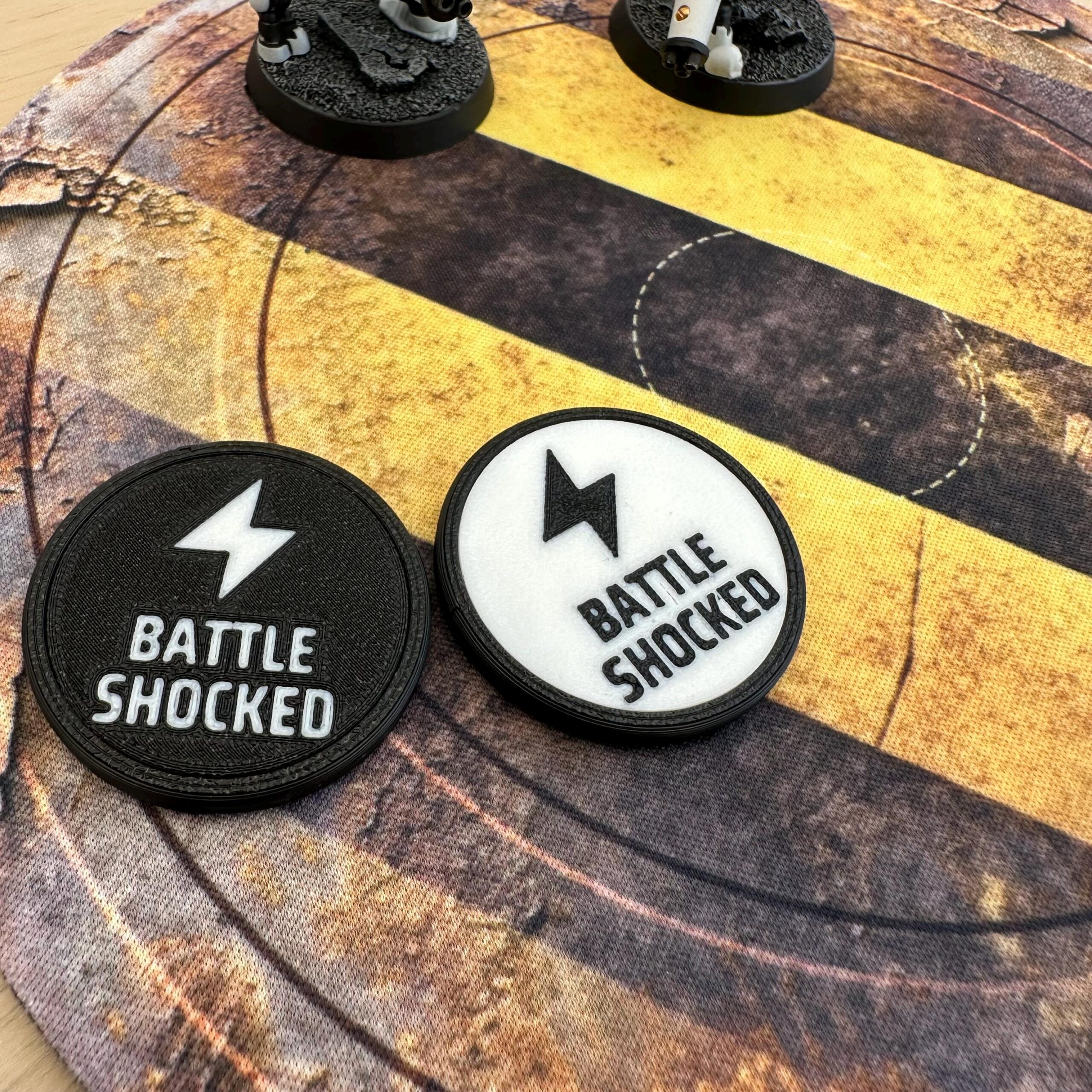 Two circular game tokens featuring a lightning bolt icon and the text BATTLE SHOCKED.