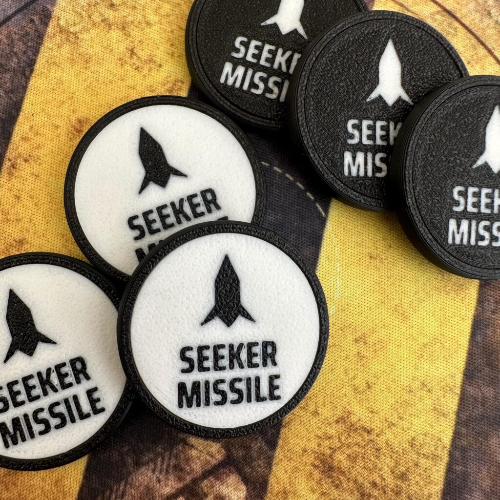 A collection of circular tokens featuring a black rocket icon above the text SEEKER MISSILE.
